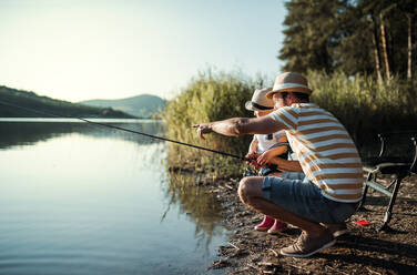 A mature father with a small toddler son outdoors fishing by a river or a lake. - HPIF20190