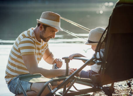 Ein erwachsener Vater mit einem kleinen Sohn im Kleinkindalter, der draußen an einem Fluss oder See angelt und sich unterhält. - HPIF20199