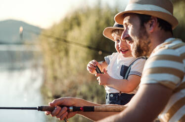 A mature father with a small toddler son outdoors fishing by a river or a lake. - HPIF20211