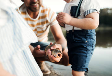 A mature father with small toddler children fishing by a river or a lake, holding a fish. - HPIF20219