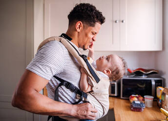 Ein Vater mit seinem kleinen Sohn im Kinderwagen in der Küche zu Hause, der Spaß hat. - HPIF20233