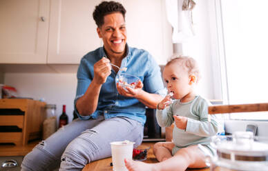 Ein Vater und sein kleiner Sohn im Kleinkindalter essen Obst und Joghurt in der Küche zu Hause. - HPIF20234