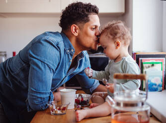 Ein Vater und sein kleiner Sohn im Kleinkindalter essen Obst und Joghurt in der Küche zu Hause. - HPIF20237
