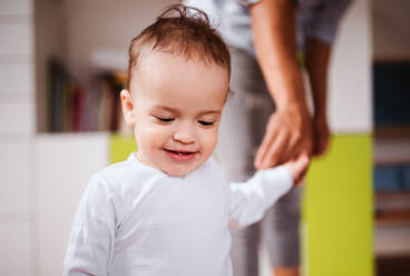 Portrait of young small toddler boy with unrecognizable parent indoors at home, walking. - HPIF20249