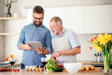 Ein Porträt eines erwachsenen Hipster-Sohns und eines älteren Vaters in der Küche zu Hause, der ein Tablet benutzt. - HPIF20274