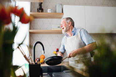 Ein älterer Mann in der Küche zu Hause, der nach dem Kochen eine Pfanne abwäscht. - HPIF20283