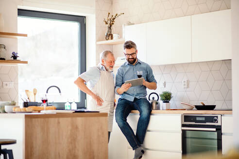 Ein Porträt eines erwachsenen Hipster-Sohns und eines älteren Vaters in der Küche zu Hause, der ein Tablet benutzt. - HPIF20289