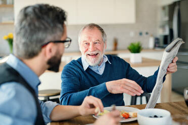 Ein erwachsener Hipster-Sohn und ein älterer Vater sitzen zu Hause am Tisch und essen ein leichtes Mittagessen. - HPIF20307