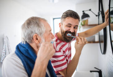 An adult hipster son and senior father brushing teeth in the bathroom indoors at home. - HPIF20326