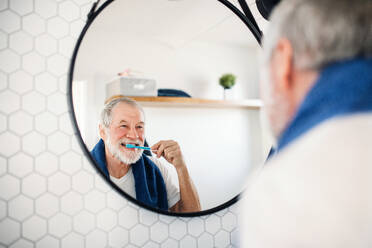Ein älterer Mann putzt sich zu Hause im Badezimmer die Zähne und schaut in den Spiegel. Kopierraum. - HPIF20330