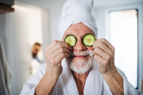 Ein älterer Mann mit Gurke vor den Augen im Badezimmer zu Hause. - HPIF20345