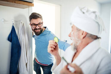 A cheerful adult hipster son and senior father in bathroom indoors at home, having fun. - HPIF20347