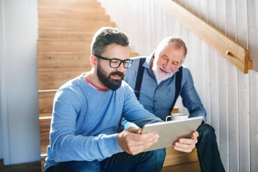 Ein erwachsener Hipster-Sohn und ein älterer Vater mit Tablet sitzen auf einer Treppe im Haus. - HPIF20361