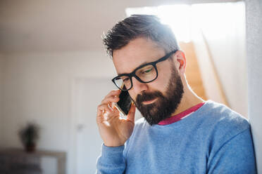 A hipster man with smartphone standing indoors at home, making a phone call. - HPIF20367