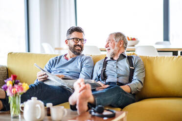 Ein erwachsener Hipster-Sohn und ein älterer Vater mit Zeitungen sitzen zu Hause auf dem Sofa und unterhalten sich. - HPIF20377