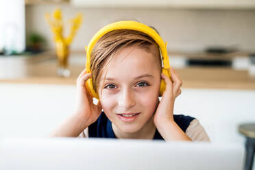 A small boy with headphones and laptop sitting at the table indoors at home. - HPIF20394