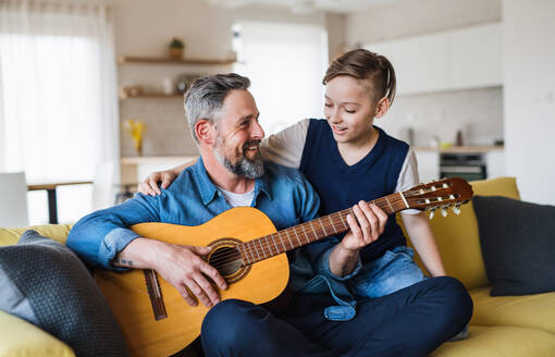 Ein reifer Vater mit seinem kleinen Sohn sitzt auf dem Sofa in einem Haus und spielt Gitarre. - HPIF20397