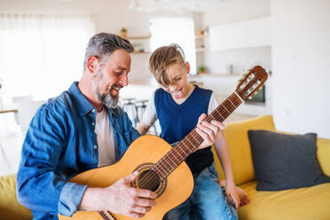 A mature father with small son sitting on sofa indoors, playing guitar.. - HPIF20398