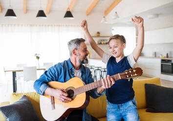 A mature father with small son sitting on sofa indoors, playing guitar. - HPIF20399