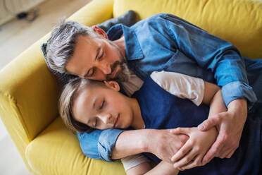 A mature father with small son lying on sofa indoors, sleeping and resting. - HPIF20400