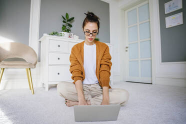 Freelancer wearing eyeglasses working on laptop at home - NLAF00033