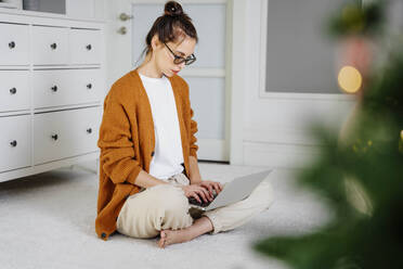 Freelancer working on laptop sitting on carpet at home - NLAF00036
