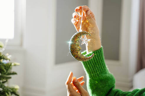 Hand of woman holding moon Christmas ornament at home - NLAF00047