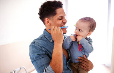 Young father and small toddler son in a bathroom indoors at home, brushing teeth. - HPIF20421