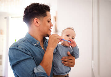 Young father and small toddler son in a bathroom indoors at home, brushing teeth. - HPIF20422