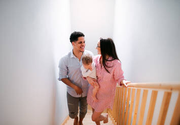 Ein Porträt einer jungen Familie mit einem kleinen Kleinkind zu Hause, das die Treppe hinaufgeht. - HPIF20462