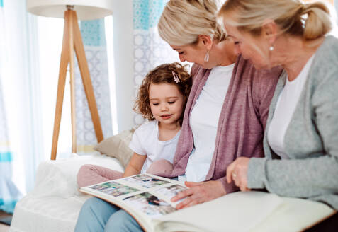 Ein kleines Mädchen mit Mutter und Großmutter sitzt zu Hause auf dem Sofa und sieht sich Fotos an. - HPIF20463
