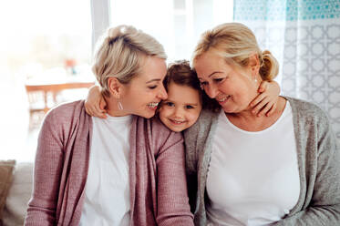 Ein Porträt eines glücklichen kleinen Mädchens mit Mutter und Großmutter zu Hause, die sich umarmen. - HPIF20464