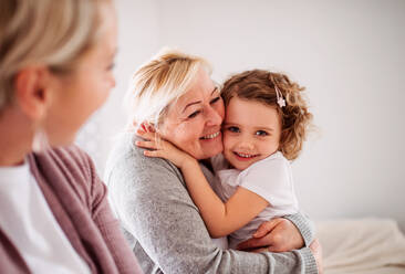 Ein Porträt eines glücklichen kleinen Mädchens mit Mutter und Großmutter zu Hause, das in die Kamera schaut. - HPIF20469