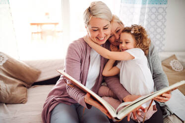 A small girl with mother and grandmother sitting on a sofa at home, looking at photographs. - HPIF20471