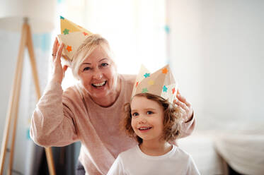 A portrait of small girl and grandmother with paper crown at home, having fun. - HPIF20507