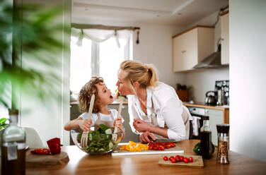 Porträt eines kleinen Mädchens mit Großmutter in einer Küche zu Hause, die einen Gemüsesalat zubereitet. - HPIF20544