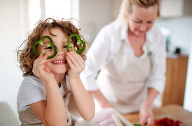 Ein Porträt eines glücklichen kleinen Mädchens mit Großmutter, das zu Hause einen Gemüsesalat zubereitet und Spaß hat. - HPIF20546