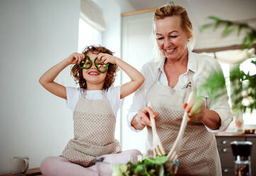 A portrait of happy small girl with grandmother preparing vegetable salad at home, having fun. - HPIF20551