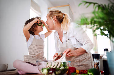 Ein Porträt eines glücklichen kleinen Mädchens mit Großmutter, das zu Hause einen Gemüsesalat zubereitet und Spaß hat. - HPIF20552