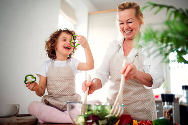 Porträt eines kleinen Mädchens mit Großmutter in einer Küche zu Hause, die einen Gemüsesalat zubereitet. - HPIF20553