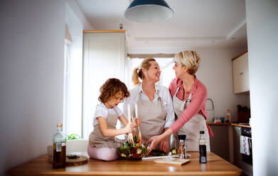 Porträt eines kleinen Mädchens mit Mutter und Großmutter zu Hause, die einen Gemüsesalat zubereiten. - HPIF20559