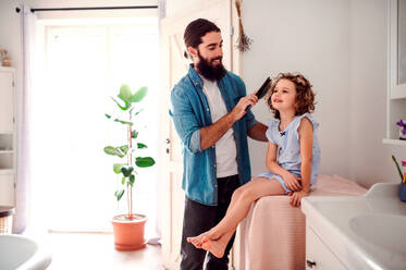 Ein junger Vater bürstet die Haare seiner kleinen Tochter im Badezimmer zu Hause. - HPIF20567