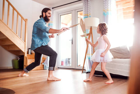 Ein kleines Mädchen und ein junger Vater mit Papierschwertern zu Hause, beim Kämpfen und Spielen. - HPIF20589