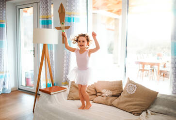 A portrait of small girl with a princess dress at home, holding a toy sword and jumping. - HPIF20590