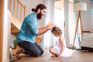 Seitenansicht eines kleinen Mädchens mit einer Prinzessinnenkrone und einem jungen Vater, der zu Hause spielt. - HPIF20591