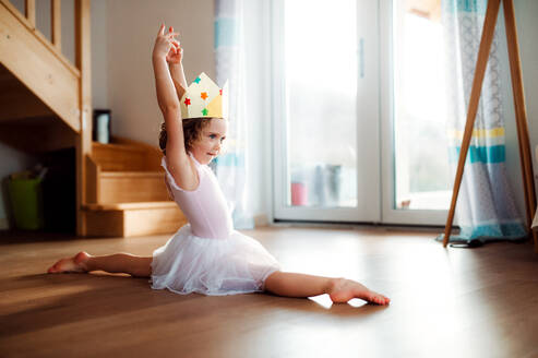 Ein kleines Ballerina-Mädchen mit einer Prinzessinnenkrone zu Hause, das Gymnastikspagat macht. - HPIF20598