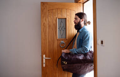 A young hipster man with bag entering front door when coming back home. - HPIF20609