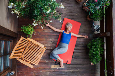 A top view of senior woman outdoors on a terrace in summer, doing exercise on mat. - HPIF20618