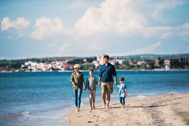 Junge Familie mit zwei kleinen Kindern läuft barfuß am Strand. - HPIF20625