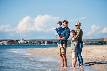 Young family with two small children standing barefoot outdoors on beach. - HPIF20626